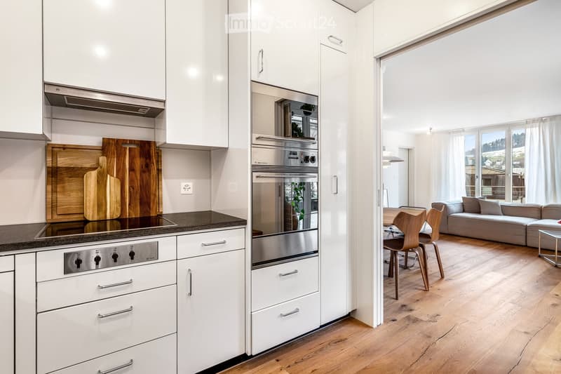 modern kitchen, white cabinets, wooden countertops, stainless steel appliances, gas stove, wooden floors, open to dining area with round table and chairs, sofa in the living room, large windows with white curtains