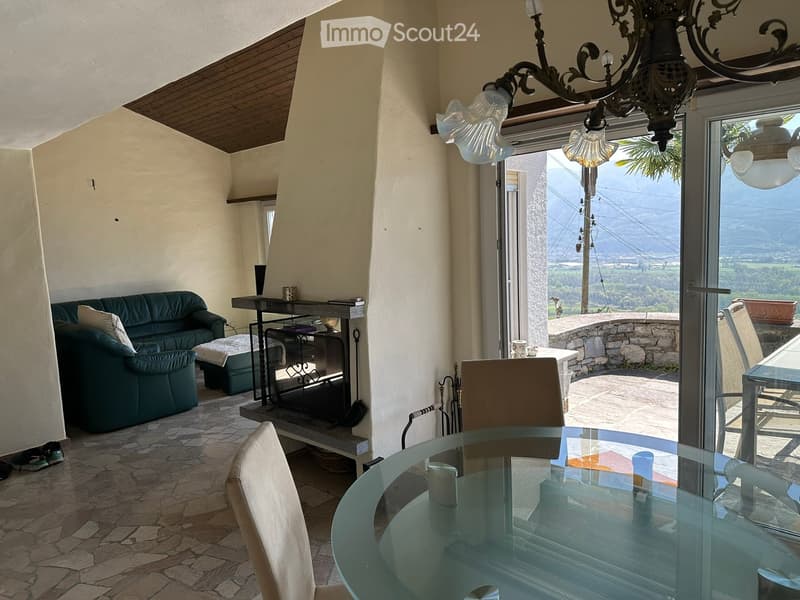 Living room with a green sofa, ottoman, coffee table, glass dining table, and chairs, overlooking a scenic valley view through large windows.
