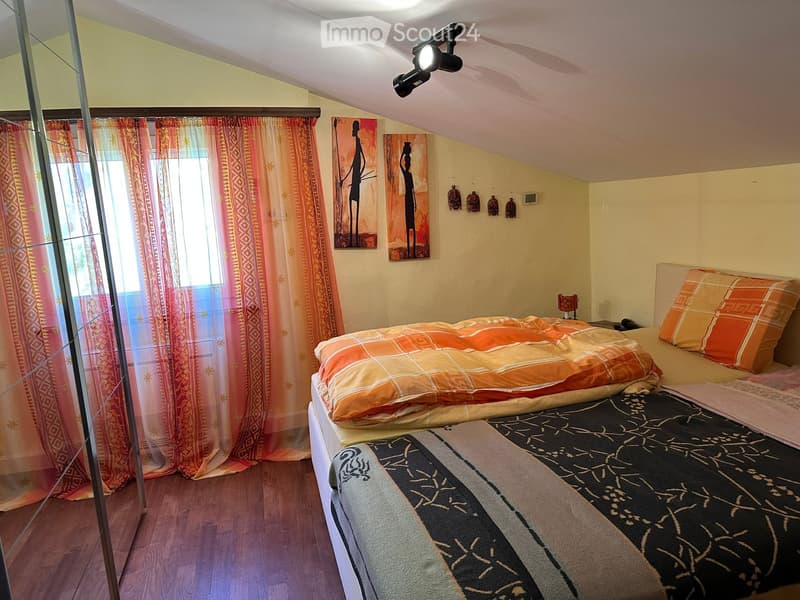Cozy bedroom with a large bed, orange and black bedding, nightstand with lamp, colorful curtains, and wall art.