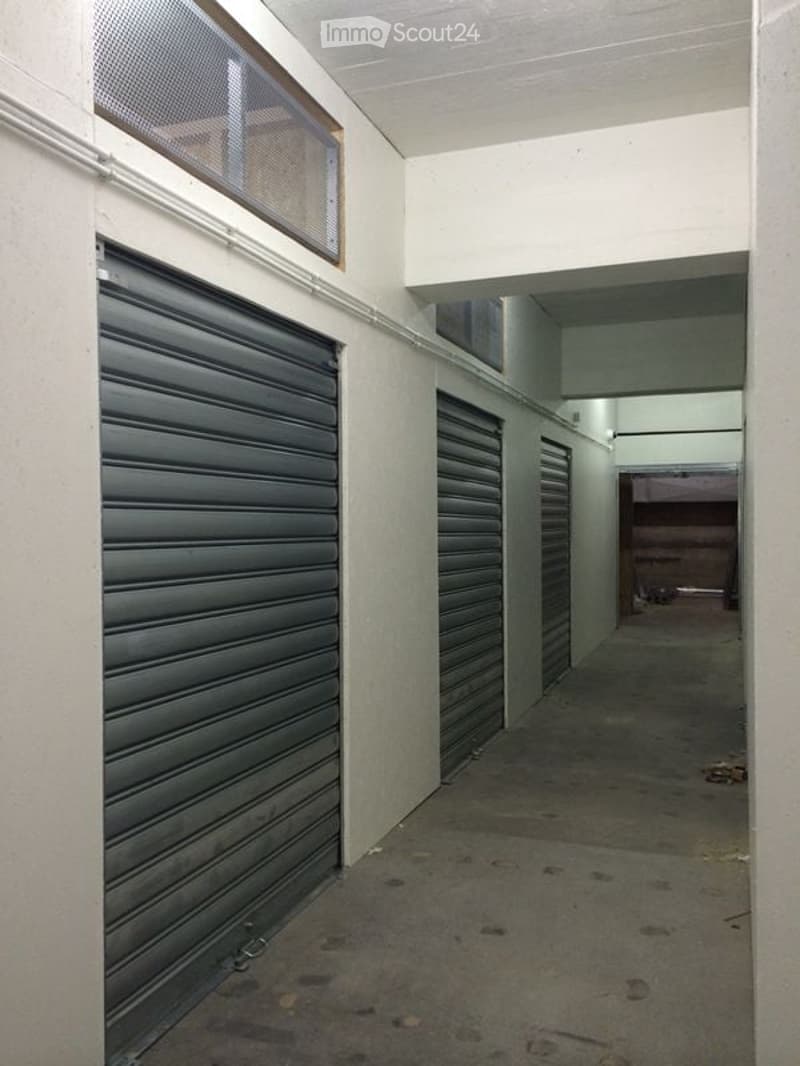 Empty storage room, metal shutters, white walls, concrete floor, two windows on the ceiling