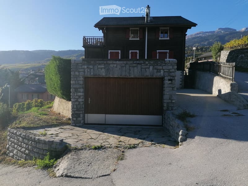 Two-story wooden house with a stone base, garage, and balcony overlooking a scenic valley.