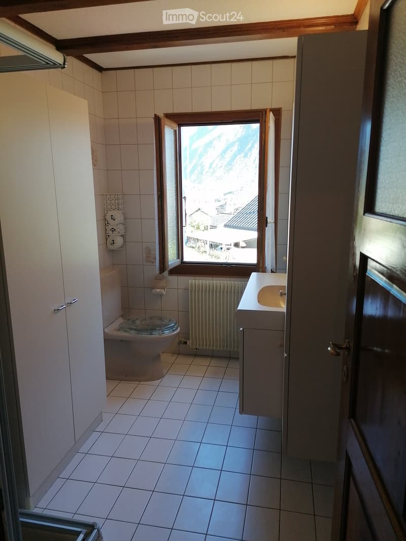 Bathroom with tiled walls and floor, toilet, sink, radiator, and a window offering a view of the surrounding area.