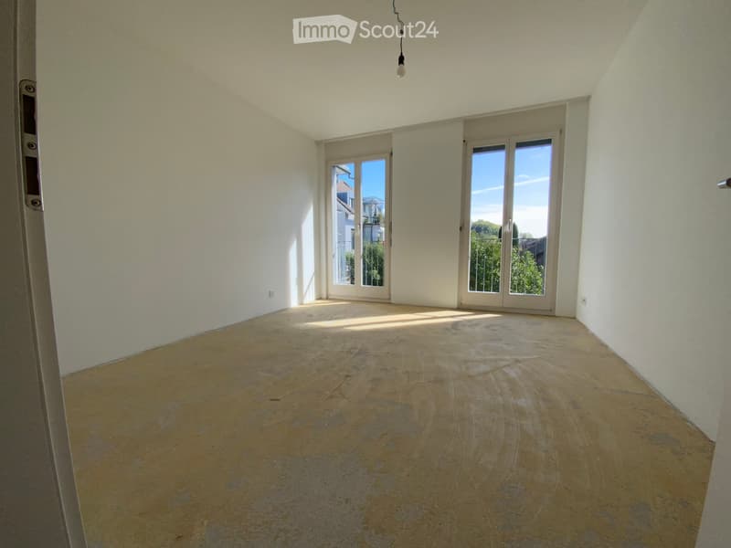 Empty room with light-colored walls, wooden floor, and large sliding glass doors leading to a balcony.
