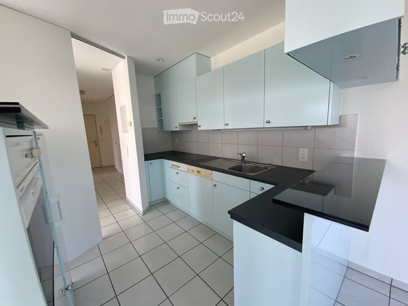 Modern kitchen with light blue cabinets, black countertops, tiled floor, and stainless steel sink.