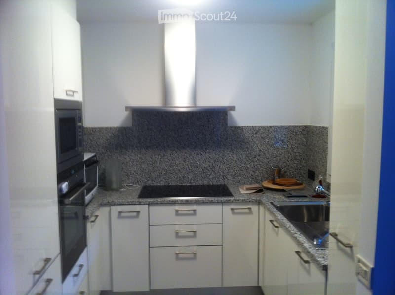 Modern kitchen with white cabinets, granite countertops, stainless steel appliances, and a built-in stove with a range hood.