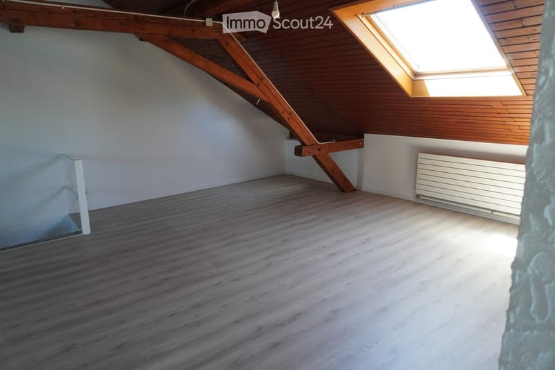Empty attic room with wooden flooring, exposed wooden beams, white walls, and a skylight window allowing natural light.