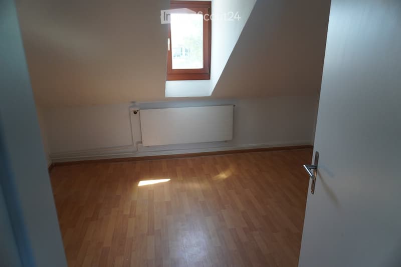 Empty room with wooden flooring, white walls, a radiator, and a window with wooden frame letting in natural light.