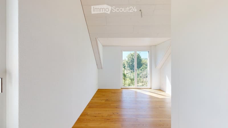 Empty room with white walls, wooden floor, and large glass doors leading to a balcony with a view of greenery.