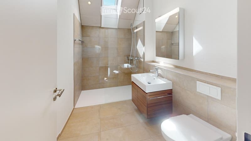 Modern bathroom with beige tiles, a glass-enclosed shower, a white sink with a wooden cabinet, a large mirror, and a toilet.