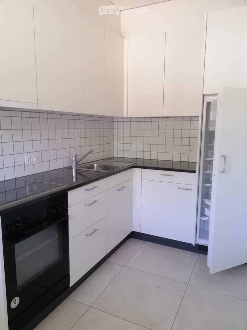 Modern kitchen with white cabinets, black countertops, stainless steel sink, and built-in oven. Features tiled backsplash and light-colored tile flooring.