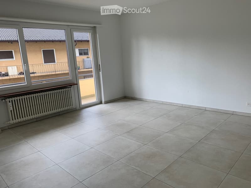 Empty room with tiled floor, white walls, large windows, and a radiator. No furniture or equipment present.