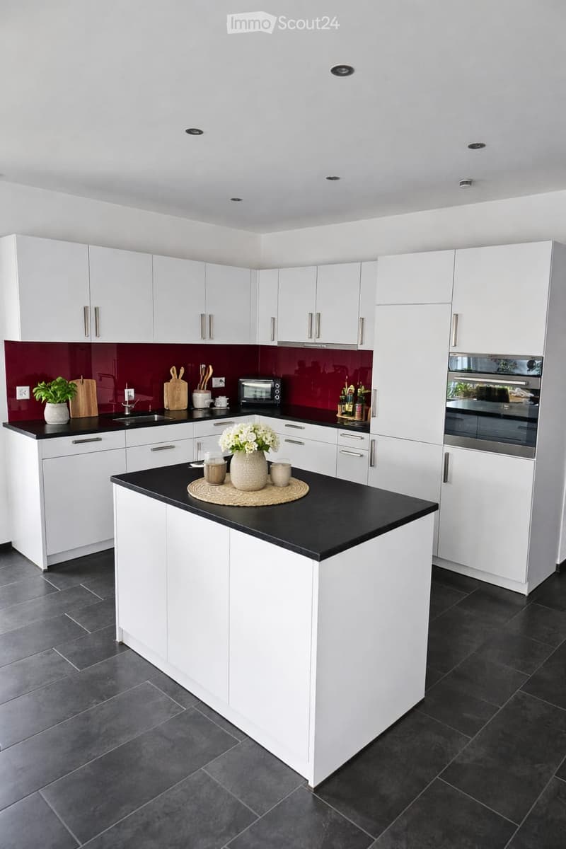 Modern kitchen with white cabinets, black countertops, and stainless steel appliances. Features a central island with a vase of flowers and cups, a sink, and a toaster on the counter.