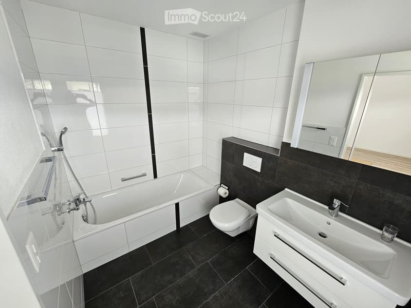 Modern bathroom with white tiles, black accents, bathtub, toilet, sink, and large mirror.