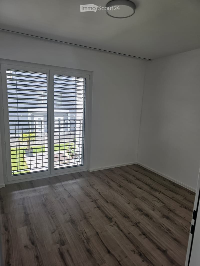 Empty room with wooden flooring, white walls, and large windows with blinds. No furniture or equipment present.