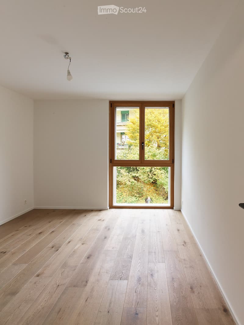 A large glass window, wood floor, white walls, small outlet.