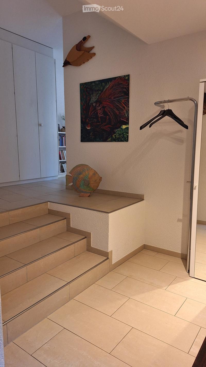 Hallway with tiled floor, staircase, wall-mounted artwork, and coat rack.