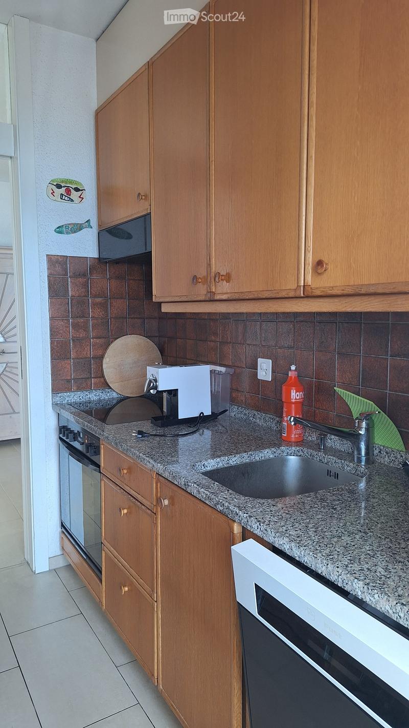 A compact kitchen with wooden cabinets, granite countertops, a sink, and various appliances including a coffee maker and a bottle on the counter.
