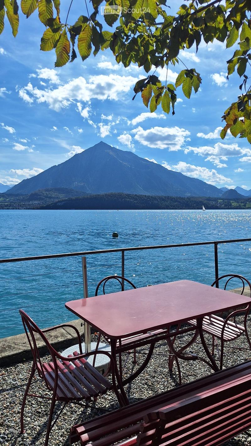 Balcony overlooking a lake with a mountain backdrop, featuring a table and chairs.