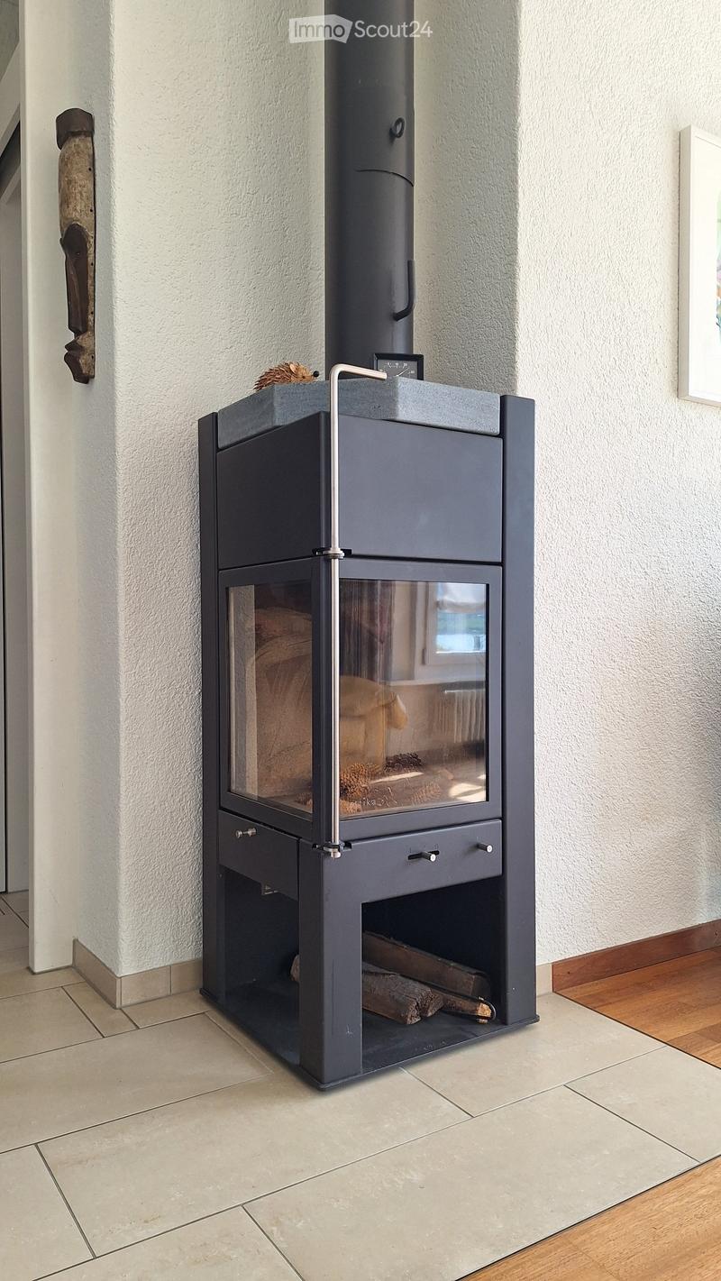 Modern black wood-burning stove with glass door and storage compartments, placed on tiled floor next to wooden flooring.