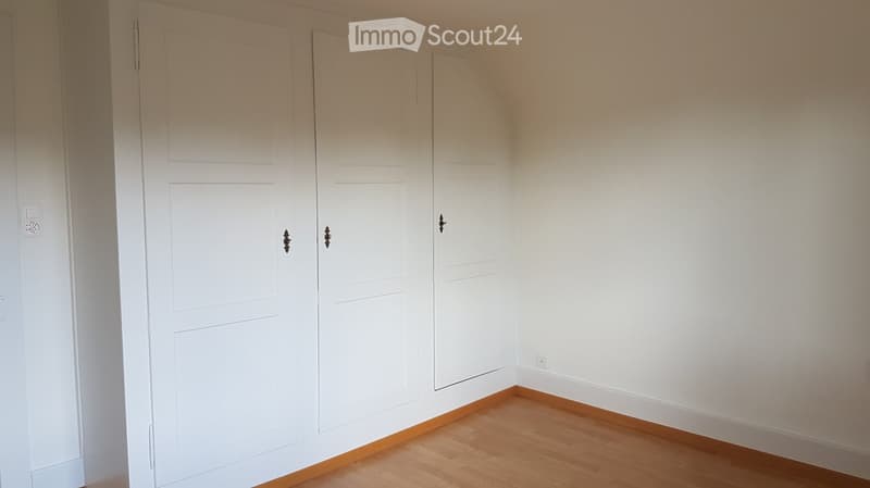 Empty room with white walls, wooden floor, and built-in white wardrobes.