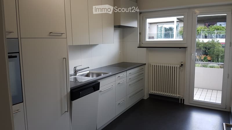 Modern kitchen with white cabinets, stainless steel sink, dishwasher, and a window overlooking a balcony area.