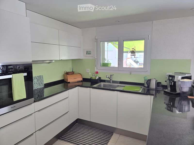 Modern kitchen with white cabinets, black countertops, stainless steel appliances, and a window overlooking a green area.