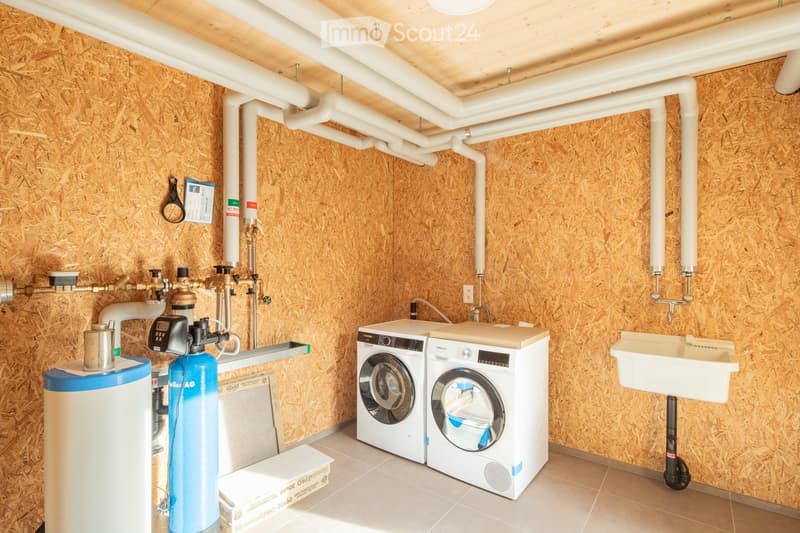 Utility room with wooden walls, white ceiling pipes, washing machine, dishwasher, water softener, and sink.