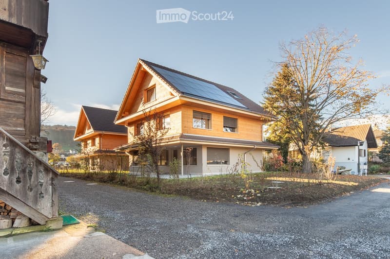 A modern two-story house with a wooden facade, solar panels on the roof, and a well-maintained garden area.