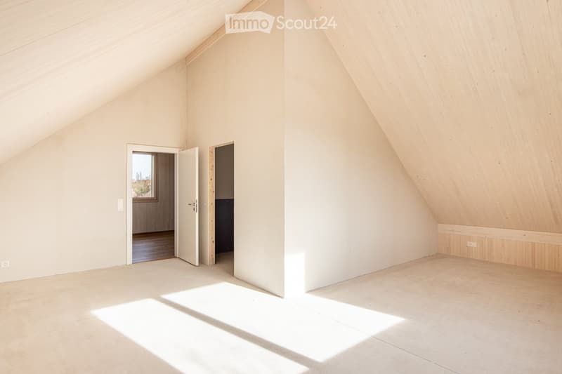 Empty attic room with wooden walls and ceiling, natural light from a window, and two open doors leading to other spaces.