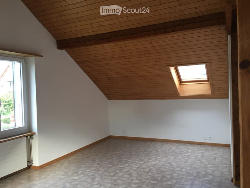 Empty attic room with wooden ceiling, tiled floor, and skylight window. Bare walls and no furniture.