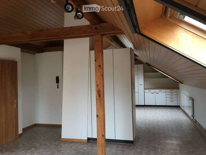 An attic space with wooden beams, white cabinets, and a tiled floor. The room features exposed wooden beams and a slanted ceiling with skylights.