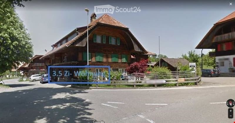 Traditional Swiss wooden house with a pitched roof, green shutters, and a sign indicating "3.5 Zi-Wohnung" (3.5 room apartment).