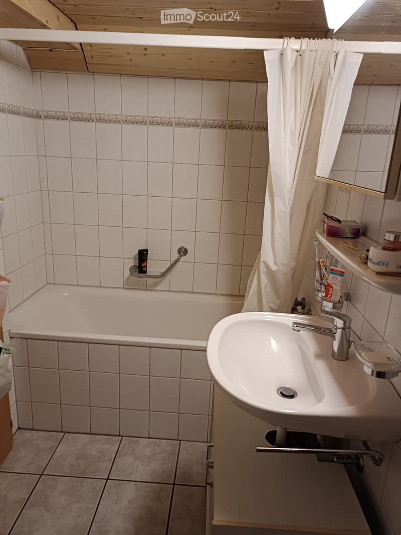 Bathroom with a bathtub, sink, mirror, and various toiletries on the sink counter.