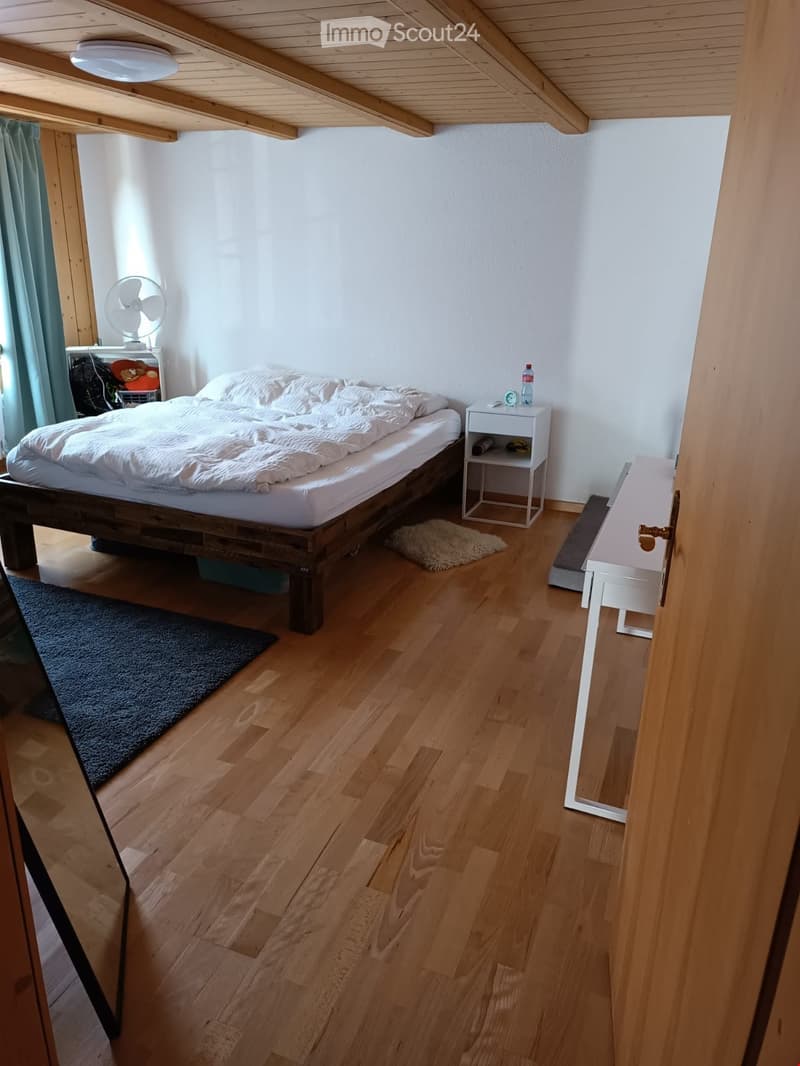 Cozy bedroom with wooden floor, bed with white bedding, nightstand, fan, and small rug.