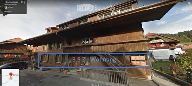 A large, traditional wooden house with multiple stories and green shutters, featuring a prominent balcony and a spacious front yard.