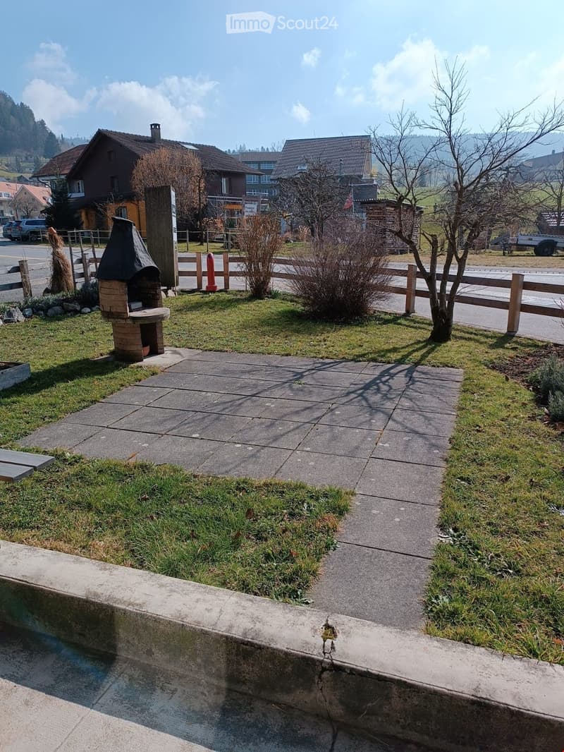 Outdoor area with a brick barbecue, wooden fence, small tree, and paved pathway.