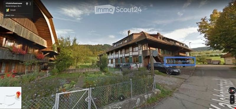 A multi-story wooden building with a traditional design, surrounded by greenery and a parking area.