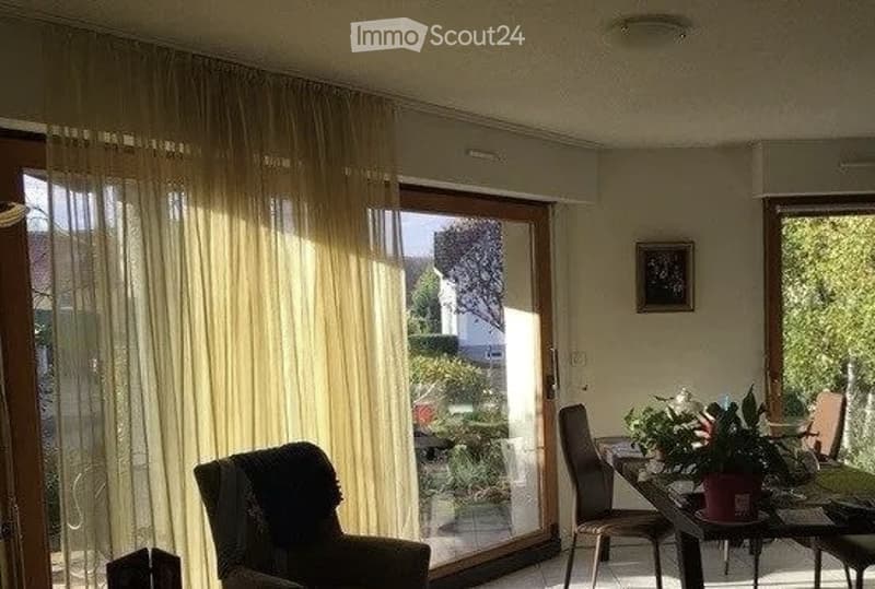 Bright living room with large sliding glass doors, sheer curtains, a sofa, a dining table with chairs, and a potted plant on the table.