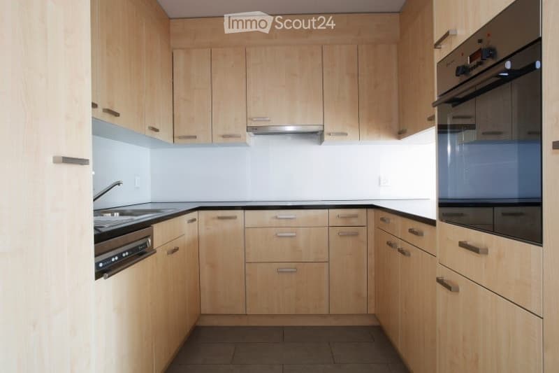 Modern kitchen with light wooden cabinets, stainless steel appliances, and a black countertop.