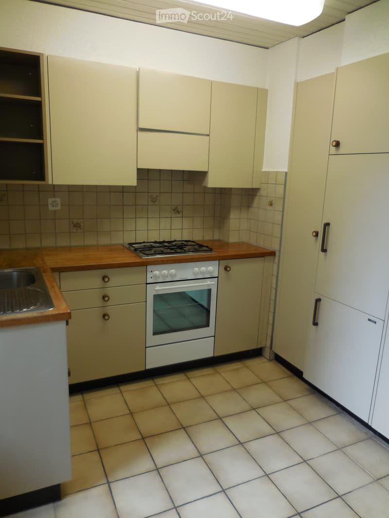 A small kitchen with light-colored cabinets, a gas stove, an oven, and a sink, featuring tiled walls and a tiled floor.