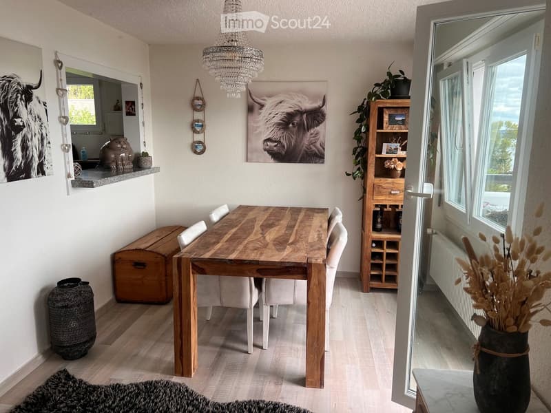 Dining room with a wooden dining table, white chairs, a wooden bookcase, and decorative items including vases and artwork.