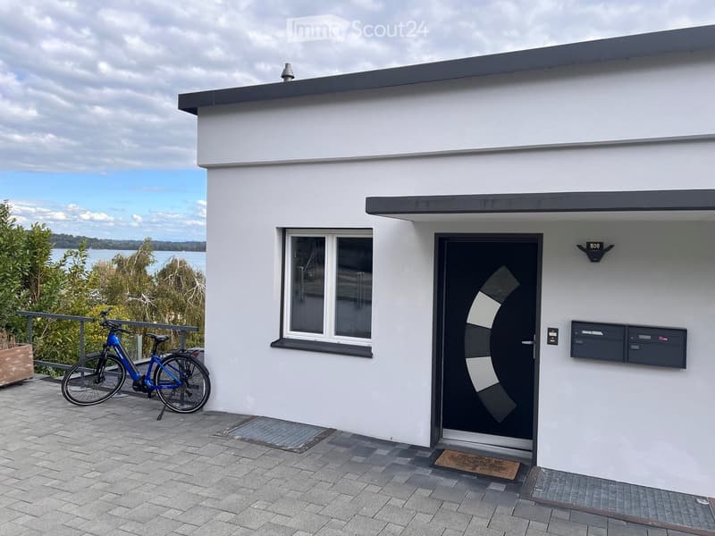 Modern white building with a flat roof, large window, and a bicycle parked on the patio.