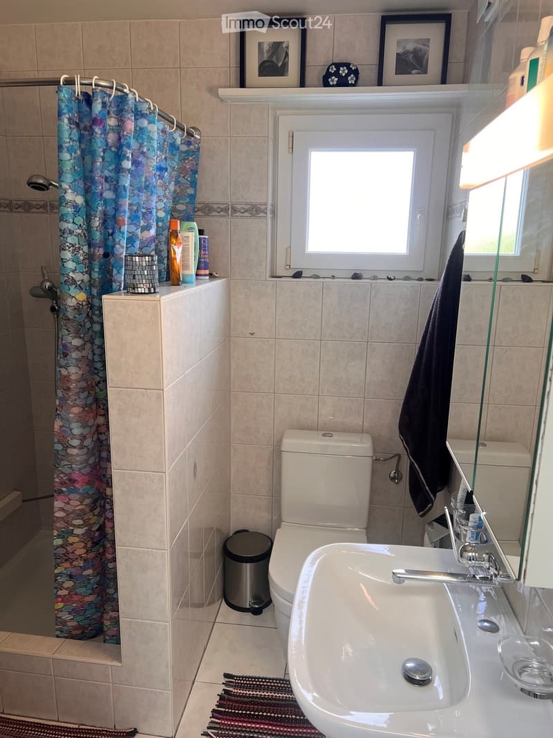 Bathroom with beige tiled walls, a toilet, a sink with a faucet, a shower curtain, a towel, a trash can, and framed pictures on the wall.
