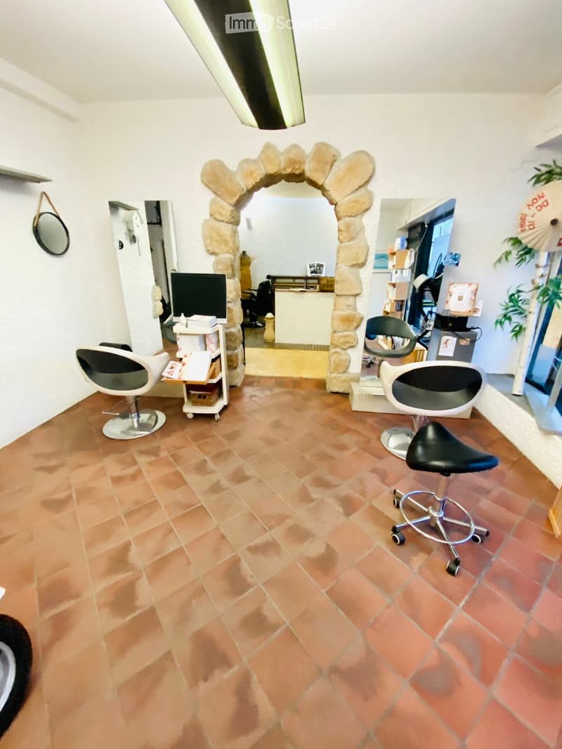 A well-lit room with terracotta tiled flooring, featuring modern chairs, a round mirror, a screen, and a small table with books and a plant in the background.