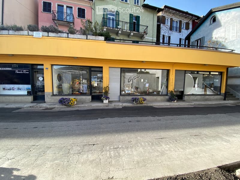 A multi-story building with a yellow storefront and several shops, including a hair salon and an architecture office, with flower pots on the sidewalk.