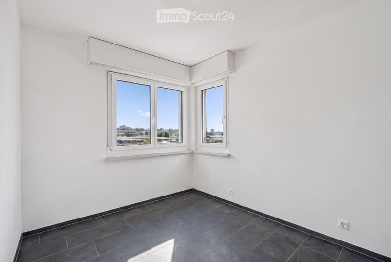 Empty room with white walls, dark tiled floor, and large windows offering a view of the outside. No furniture or equipment is present.