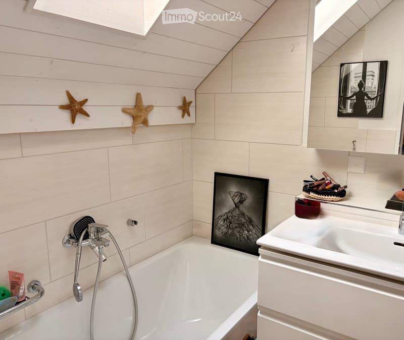 Modern bathroom with white tiled walls, a bathtub with a handheld shower, a sink with a mirror, and decorative framed artwork and star-shaped wall decorations.