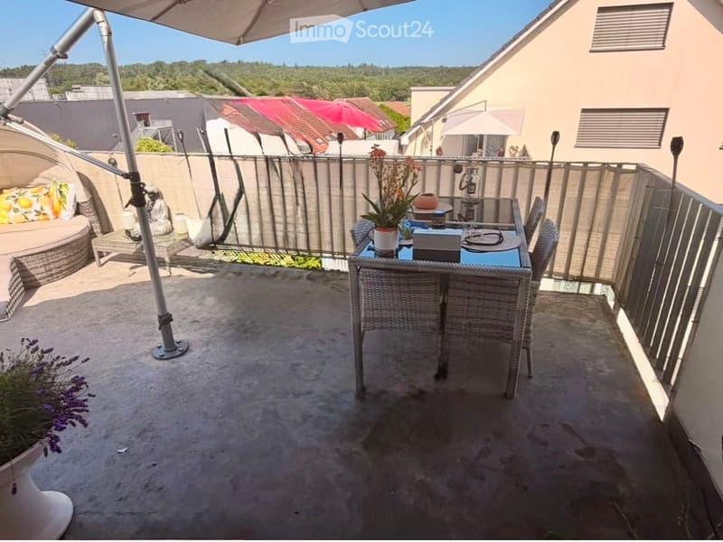 Balcony with a dining table, chairs, a sofa, and flower pots, featuring a view of the surrounding area.
