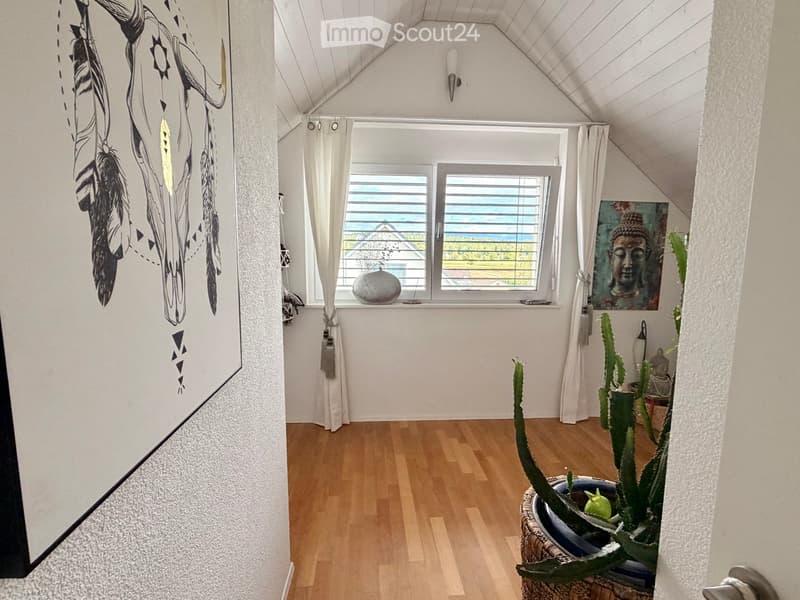 Bright, airy room with wooden flooring, large window with white curtains, cactus plant, artwork, and decorative ball on windowsill.