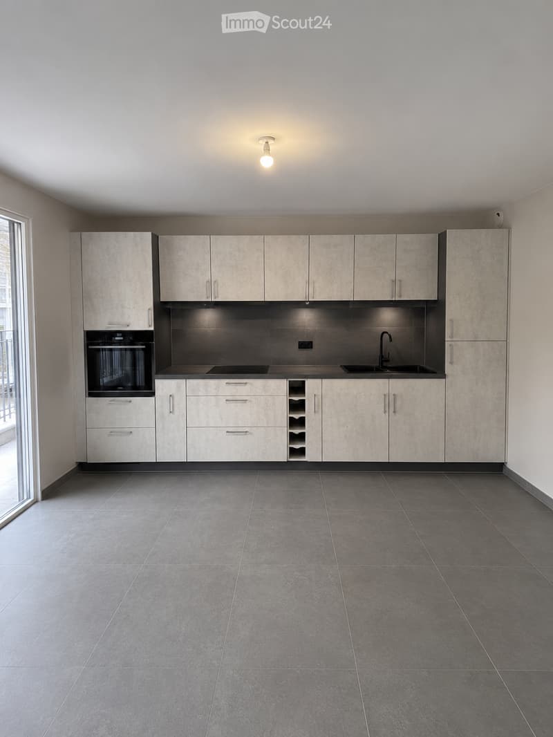 Empty kitchen with modern cabinets, stainless steel sink, and built-in oven. Grey tiled floor and white walls.